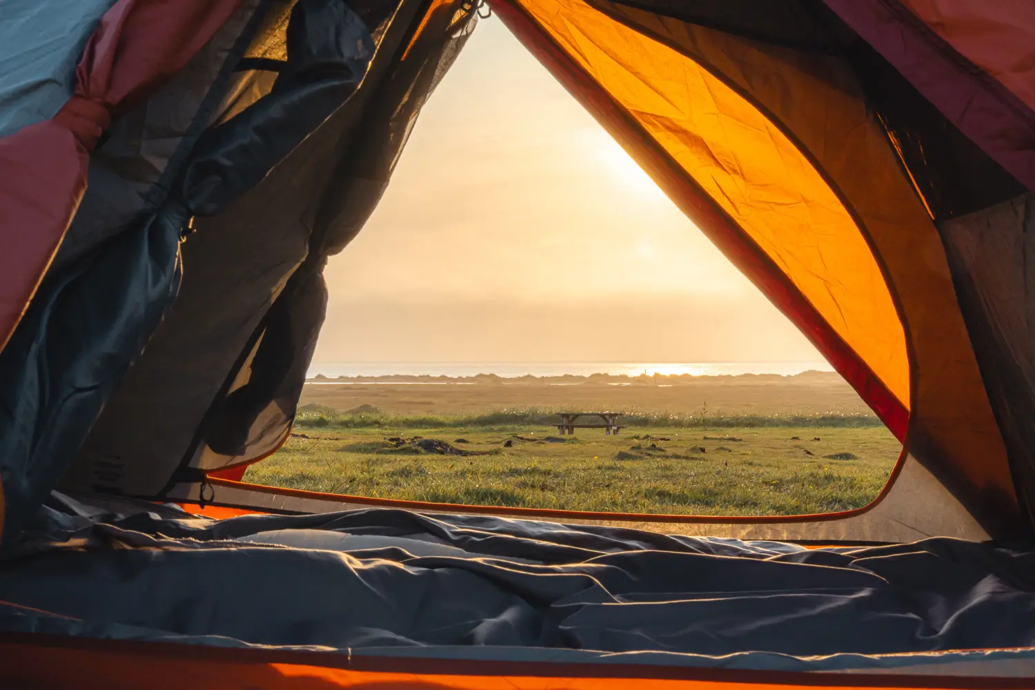 Vista, a través de las puertas de la tienda de campaña, del atardecer con el sol de verano en Islandia. Se ve la playa al final del camping.