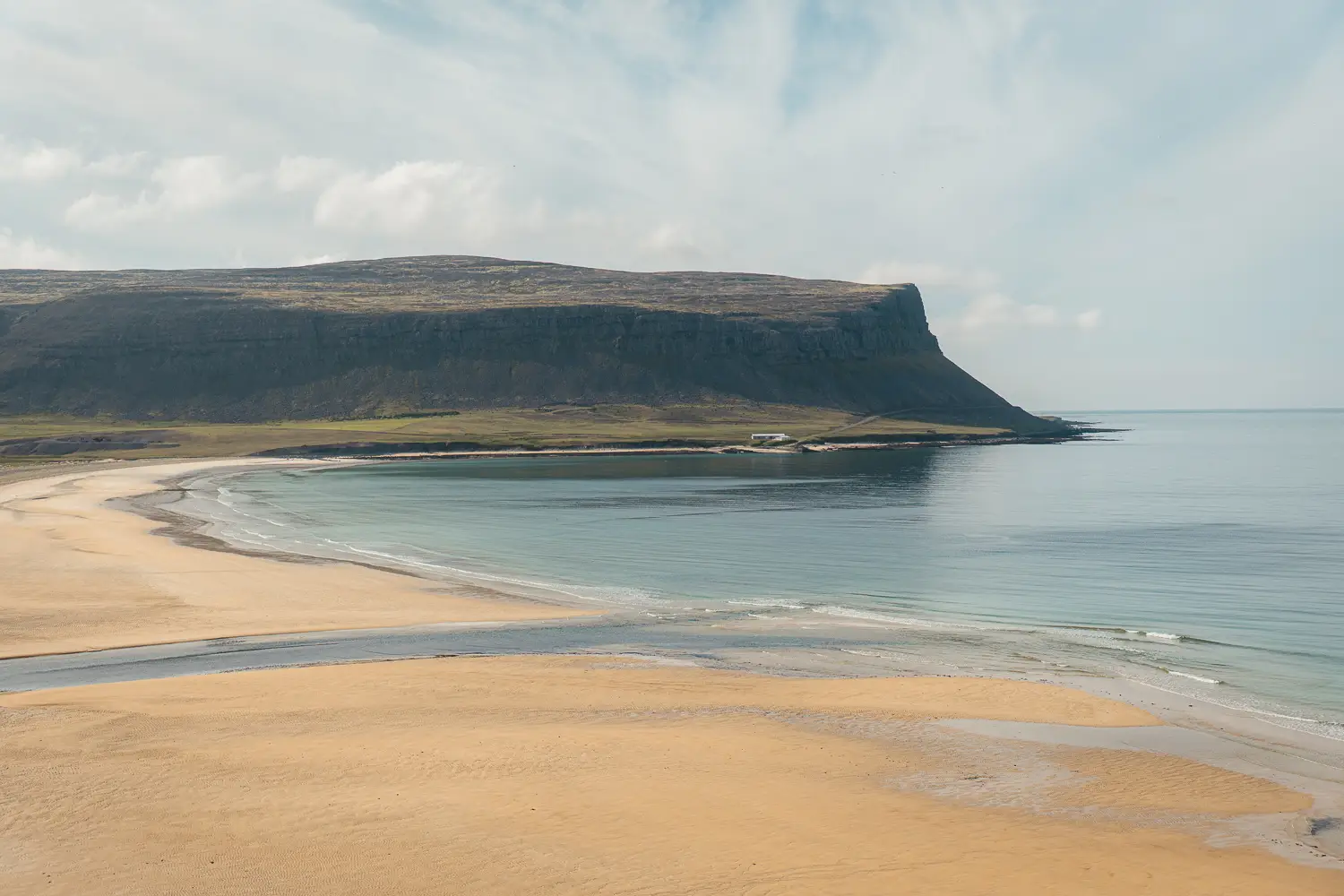 extensa playa de arena dorada y agua azulada con la montaña típica de los fiordos de fondo