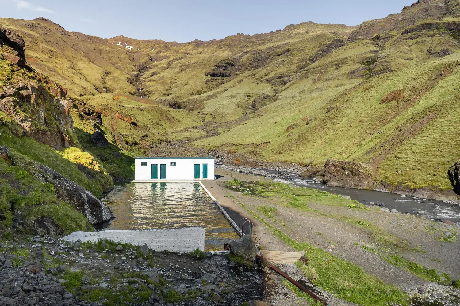 Piscina termal de Seljavallalaug dentro de un cañón con montañas verdes alrededor, un clásico en una ruta por Islandia