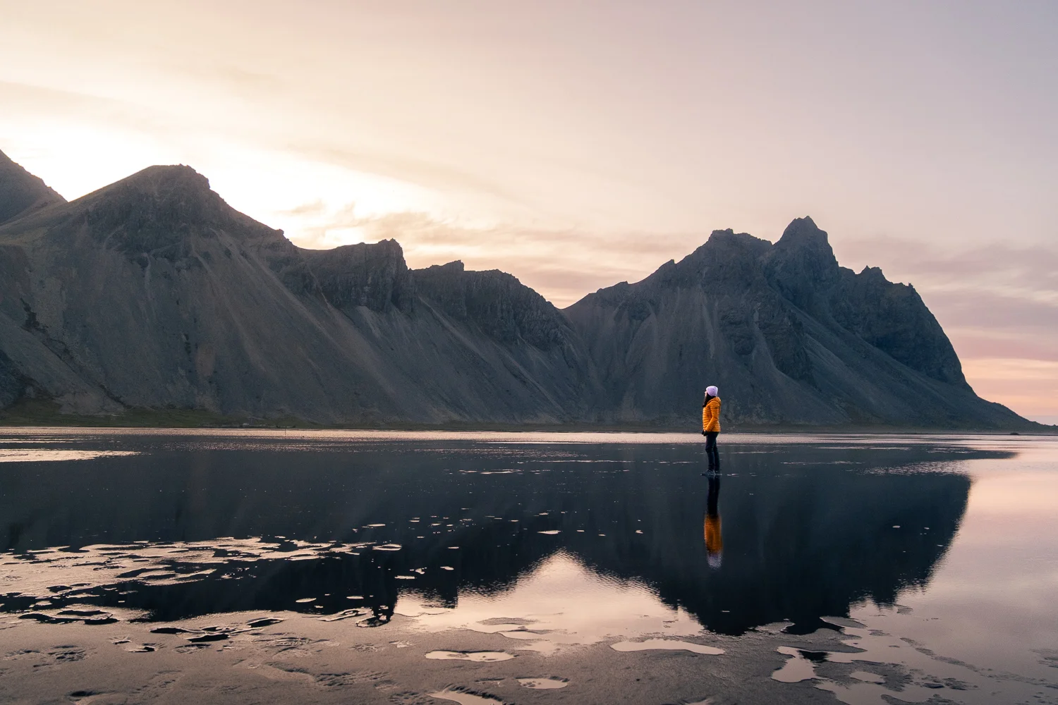 Playa de Stokksnes con marea alta y cielo rosado al atardecer de verano, frente a las montañas Vestrahorn, en Islandia.