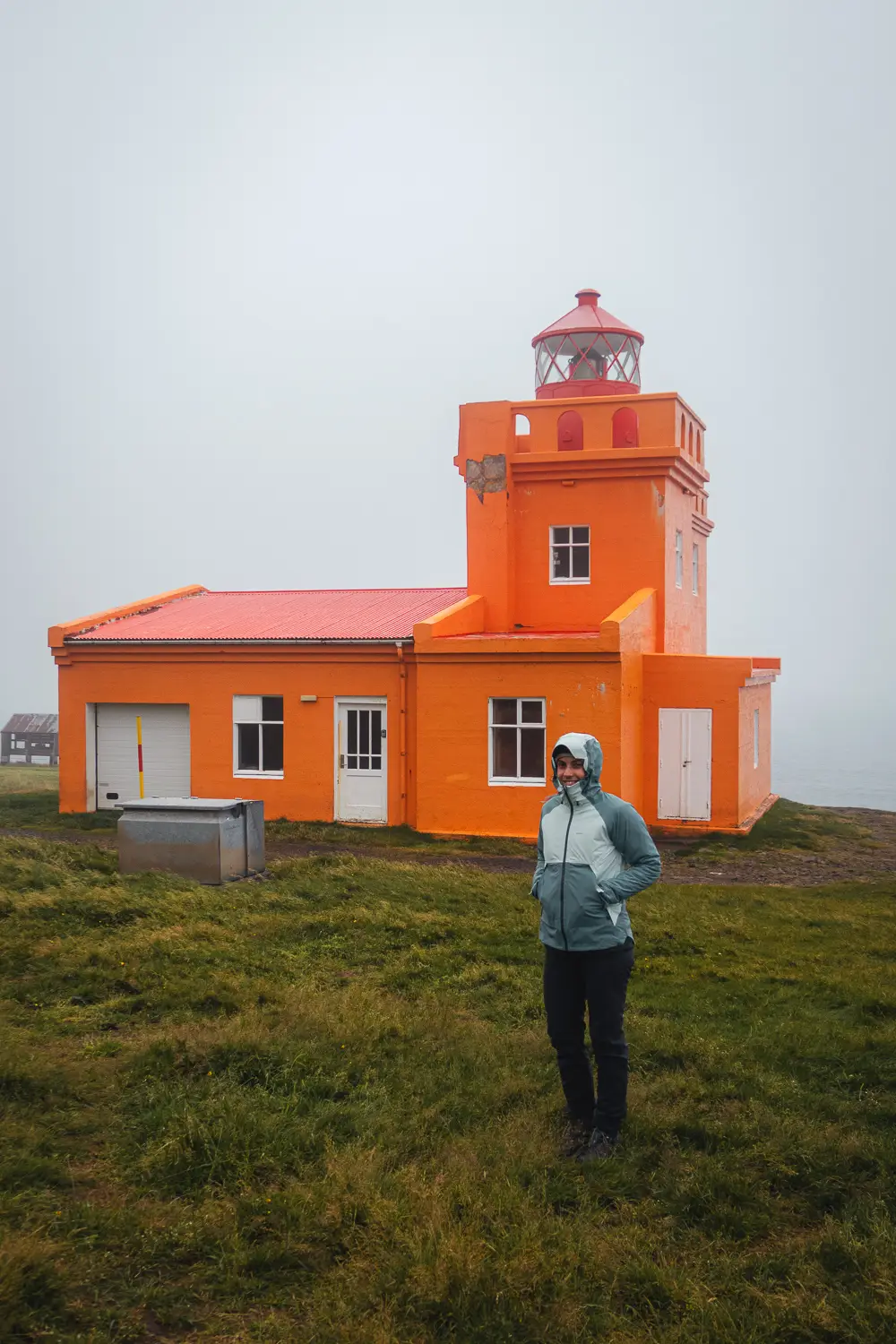 Silvia junto al faro naranja de Tröllaskagi, rodeado de niebla y viento en la costa norte de Islandia.