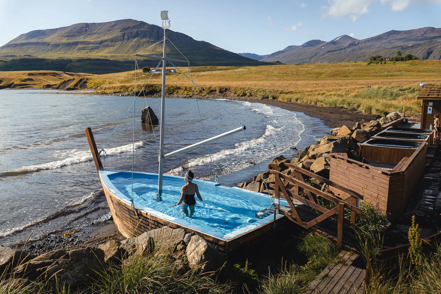 Silvia en los Hauganes Hot Tubs, disfrutando de un baño caliente con la playa y el fiordo de Eyjafjörður al fondo.