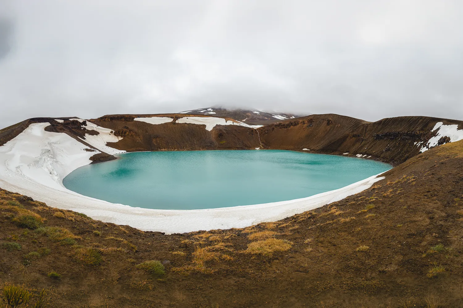 Cráter volcánico de Krafla seminevado con un lago de color turquesa, uno de los paisajes volcánicos más sorprendentes que ver en el norte de Islandia.