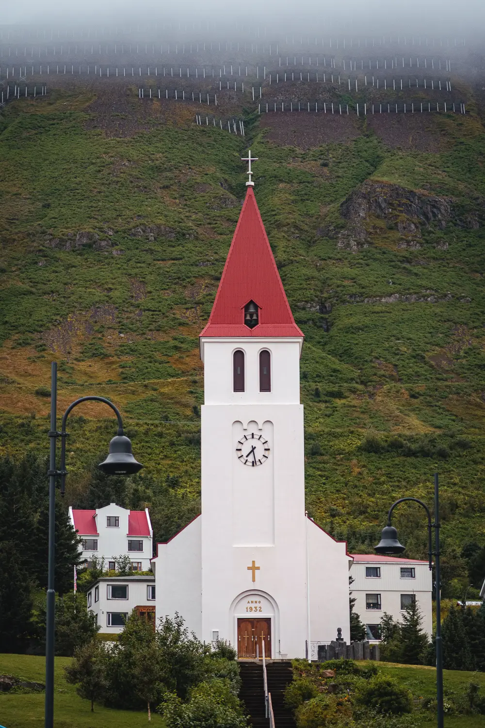 Iglesia de Siglufjörður con su característica arquitectura y una montaña verde al fondo, en un pintoresco pueblo del norte de Islandia.
