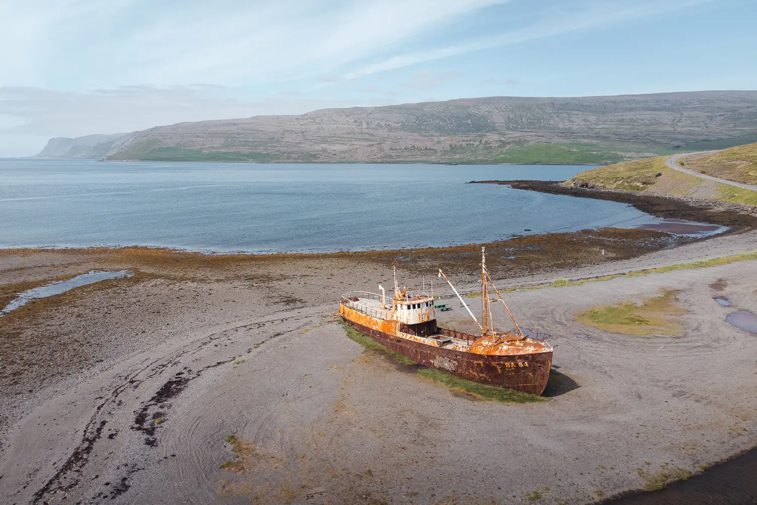 Vista de dron de una playa en un fiordo donde está el barco semi oxidado Garðar BA 64 y varado en la arena marrón.
