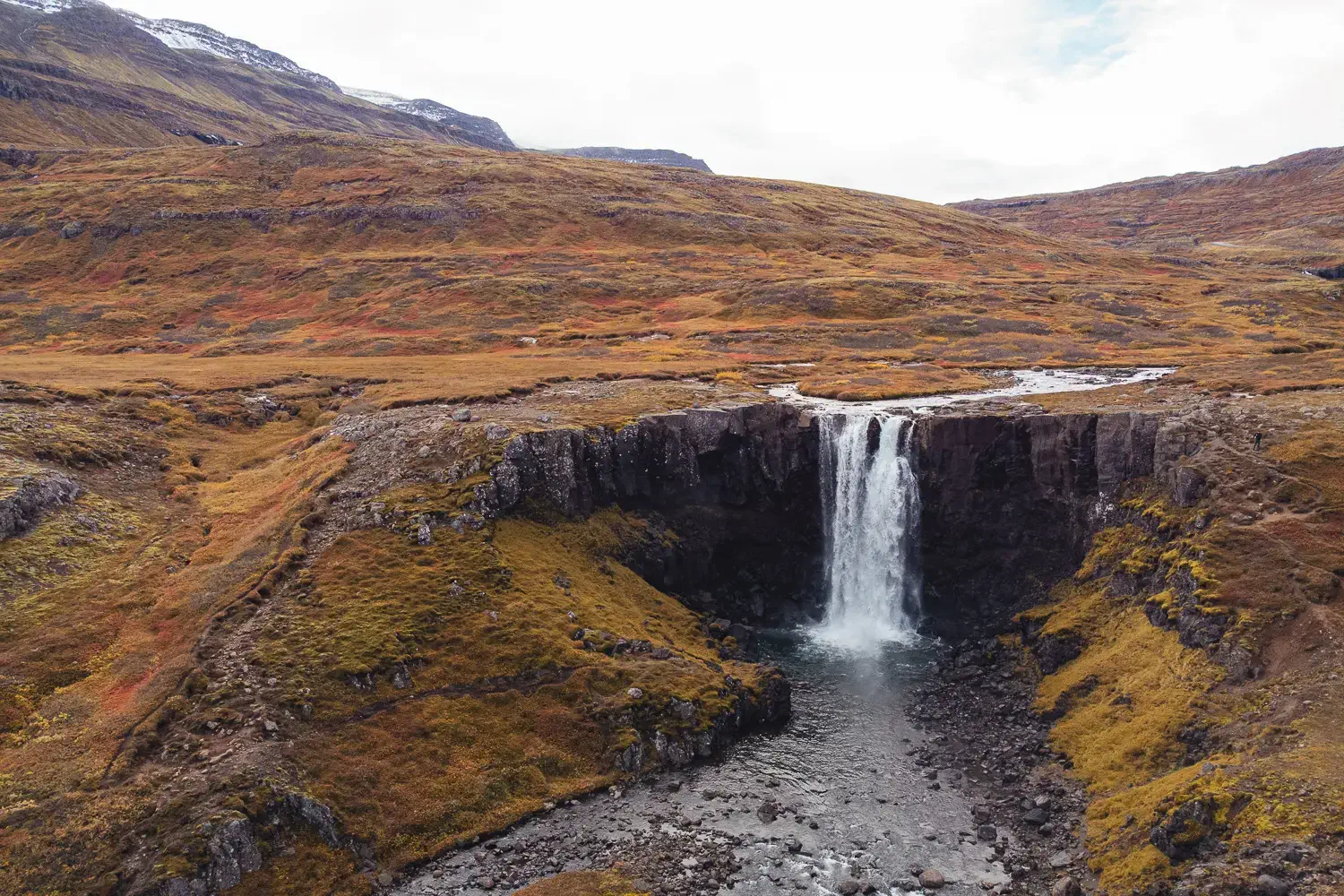 Vista de dron de Gufufoss rodeada de montañas y vegetación en tonos ocres durante el otoño, en el este de islandia