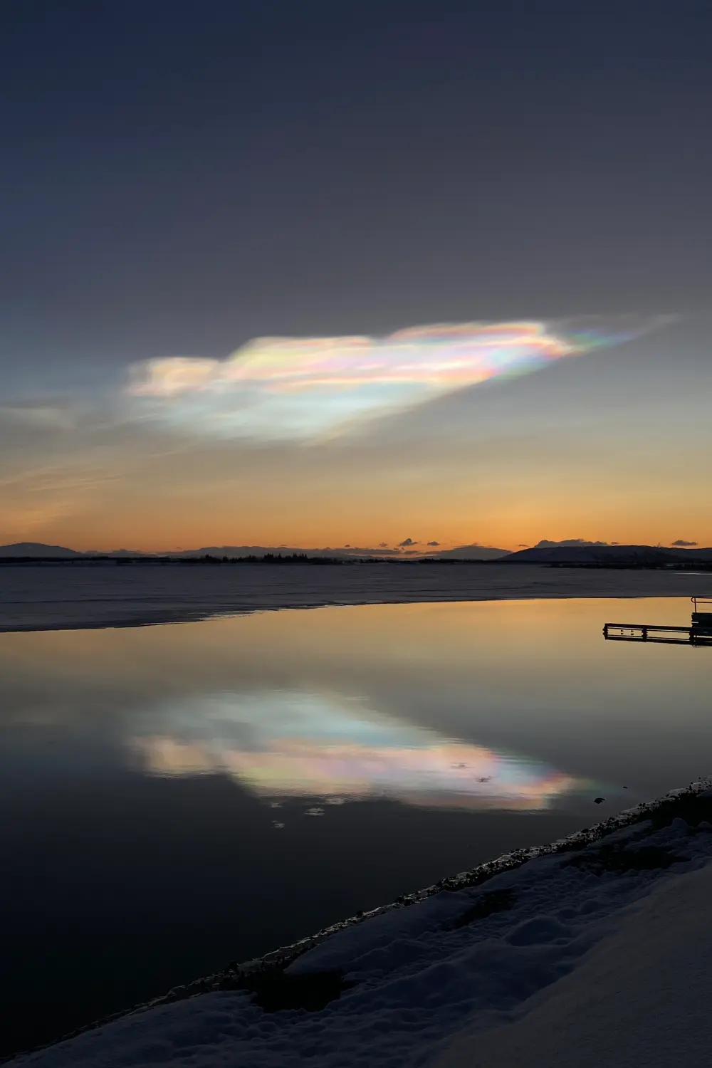 Nubes estratosféricas polares que se ven de colores como arco iris, con el reflejo de esta en el lago.